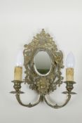 A brass two branch wall sconce with an oval mirror flanked by cherubs, converted for electricity,