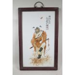 A Chinese polychrome porcelain panel decorated with a red robed Immortal, mounted in hardwood frames