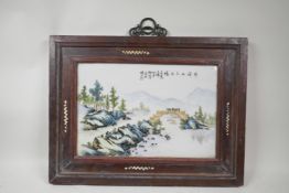 A Chinese famille verte porcelain panel depicting a riverside landscape, mounted in a hardwood frame