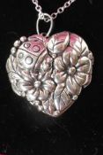 A heart shaped silver locket embossed with roses on a silver chain