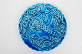 An Islamic blue glazed pottery saucer with raised script decoration, 7" diameter