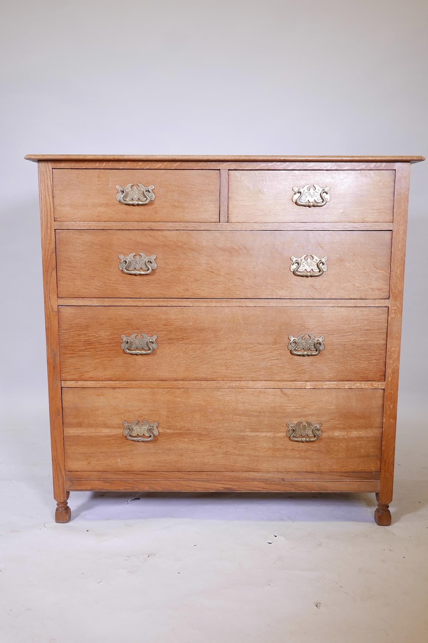 An early C20th oak chest of two over three drawers, with brass handles, raised on carved stile