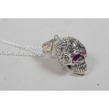 A silver pendant necklace in the form of a skull with red stone eyes