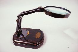 A small table top brass magnifying glass on a polished wooden base, glass 3" diameter