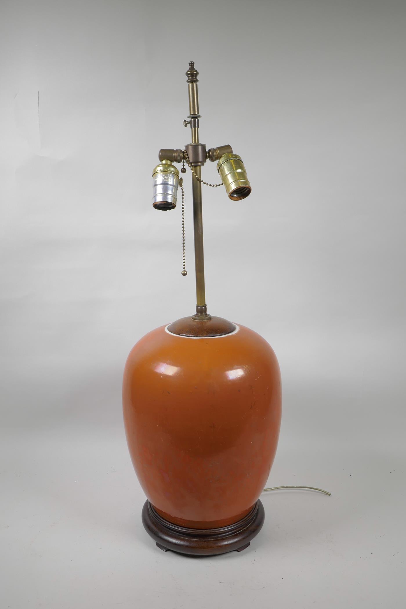 An Oriental coral glazed porcelain lamp with brass fittings on a hardwood base, 26" high