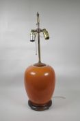 An Oriental coral glazed porcelain lamp with brass fittings on a hardwood base, 26" high