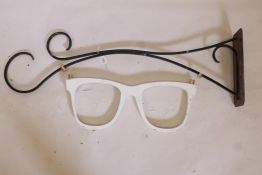 A shop front optician's sign made as a pair of wooden glasses, one wrought iron bracket, 43½" long