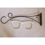 A shop front optician's sign made as a pair of wooden glasses, one wrought iron bracket, 43½" long