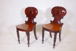 A pair of early C19th mahogany hall chairs with carved and shaped backs, and seats in the Grecian