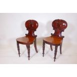 A pair of early C19th mahogany hall chairs with carved and shaped backs, and seats in the Grecian