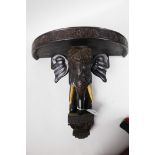 An Oriental carved ebonised wall bracket carved as a elaborately dressed elephant, 13" wide, 11½"