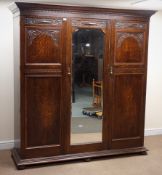 Early 20th century oak triple wardrobe, projecting cornice above three doors with carved detailing,