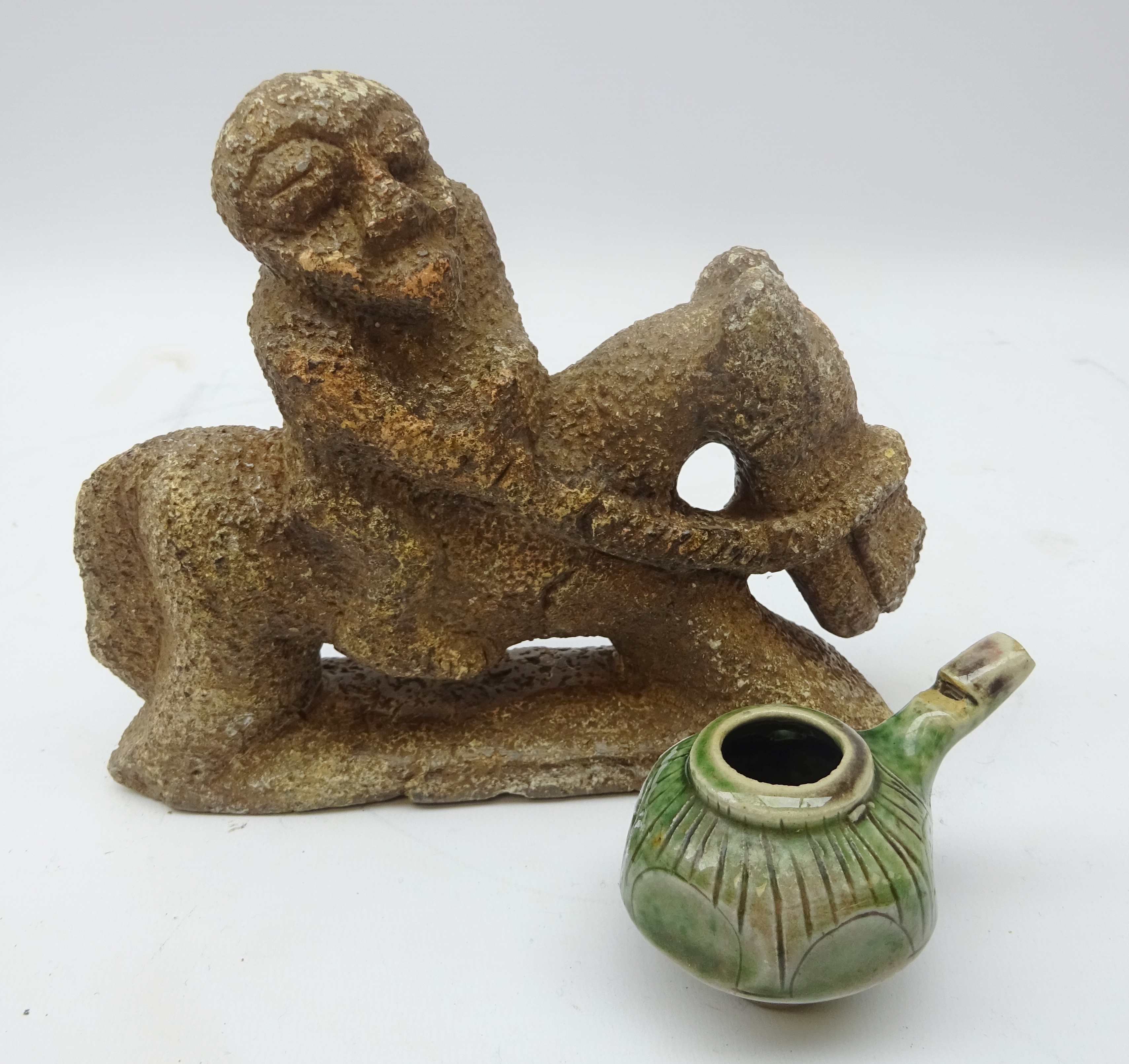 Islamic earthenware green glaze whistle and stone tribal carving of a figure on horseback,