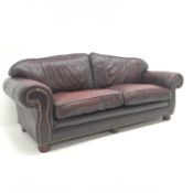 Three seat sofa upholstered in studded oxblood leather, arched back, scrolled arms,