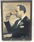 Half length portrait photograph of Victor Oliver seated in dinner jacket smoking a pipe,