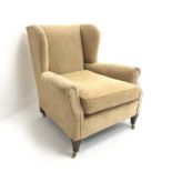 Edwardian low wingback armchair, upholstered in a beige fabric,
