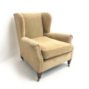 Edwardian low wingback armchair, upholstered in a beige fabric,