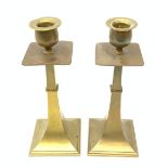 A pair of Aesthetic movement brass candlesticks, the square stepped bases leading to a tapering stem