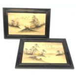 A pair of Japanese artworks, each depicting a landscape and heightened with gilt, in glazed ebonised