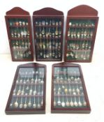 Five glazed wall display cases containing a selection of various souvenir spoons, comprising mostly