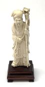 A Chinese carved ivory okimono, modelled as a sage holding a staff, raised upon a wooden base, overa