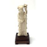 A Chinese carved ivory okimono, modelled as a sage holding a staff, raised upon a wooden base, overa