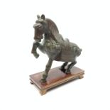 A bronze Tang style horse, modelled seated with one front leg raised, upon rectangular wooden base,