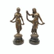 A pair of bronze figures, modelled as females in classical dress, each raised upon circular stepped