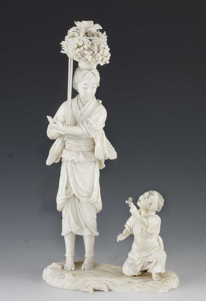 A 9" ivory okimono of a mother carrying carrying a bundle of sticks being handed a butterfly