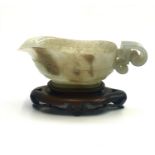 A Chinese carved jade libation cup, possibly 18th century, with a wooden stand, height 4cm, length