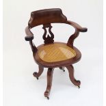 A Victorian mahogany captains office chair, with swivel rattan seat on downswept legs.Condition