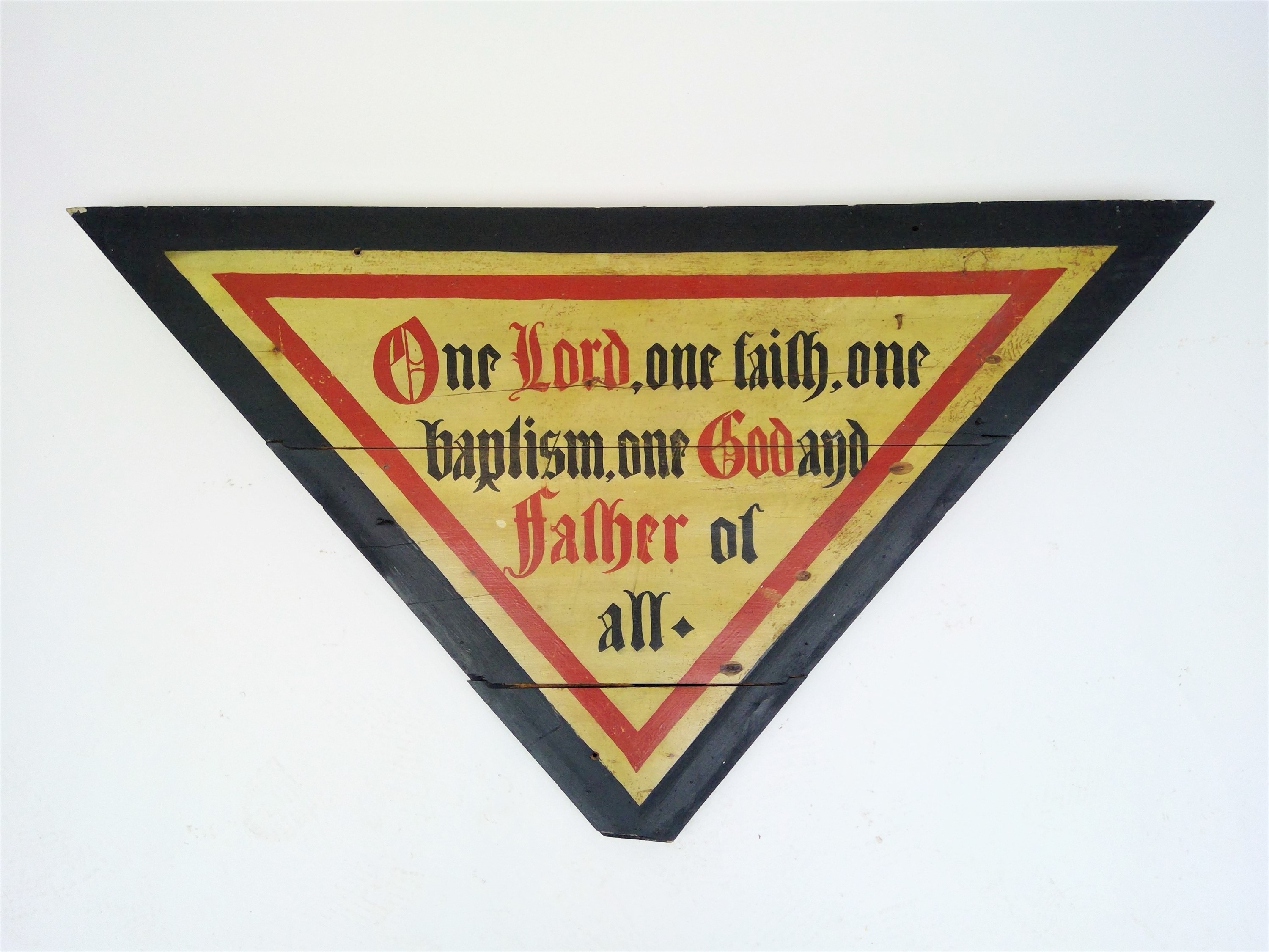 A painted wooden panel of inverted triangular form, inscribed 'One Lord, one faith, one baptism, one