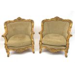 A pair of ornate gilt armchairs, early 20th Century in the French taste, the top rails with carved