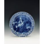 A 20th century Delft charger, painted with a mother and child in a cottage interior, within a floral