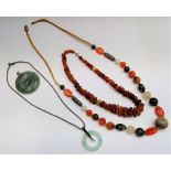Two Chinese jade bi pendants, an amber necklace and a Chinese necklace with carved hardstone beads