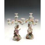 A pair of late 19th/early 20th century German porcelain candlesticks, each modelled with a figure of