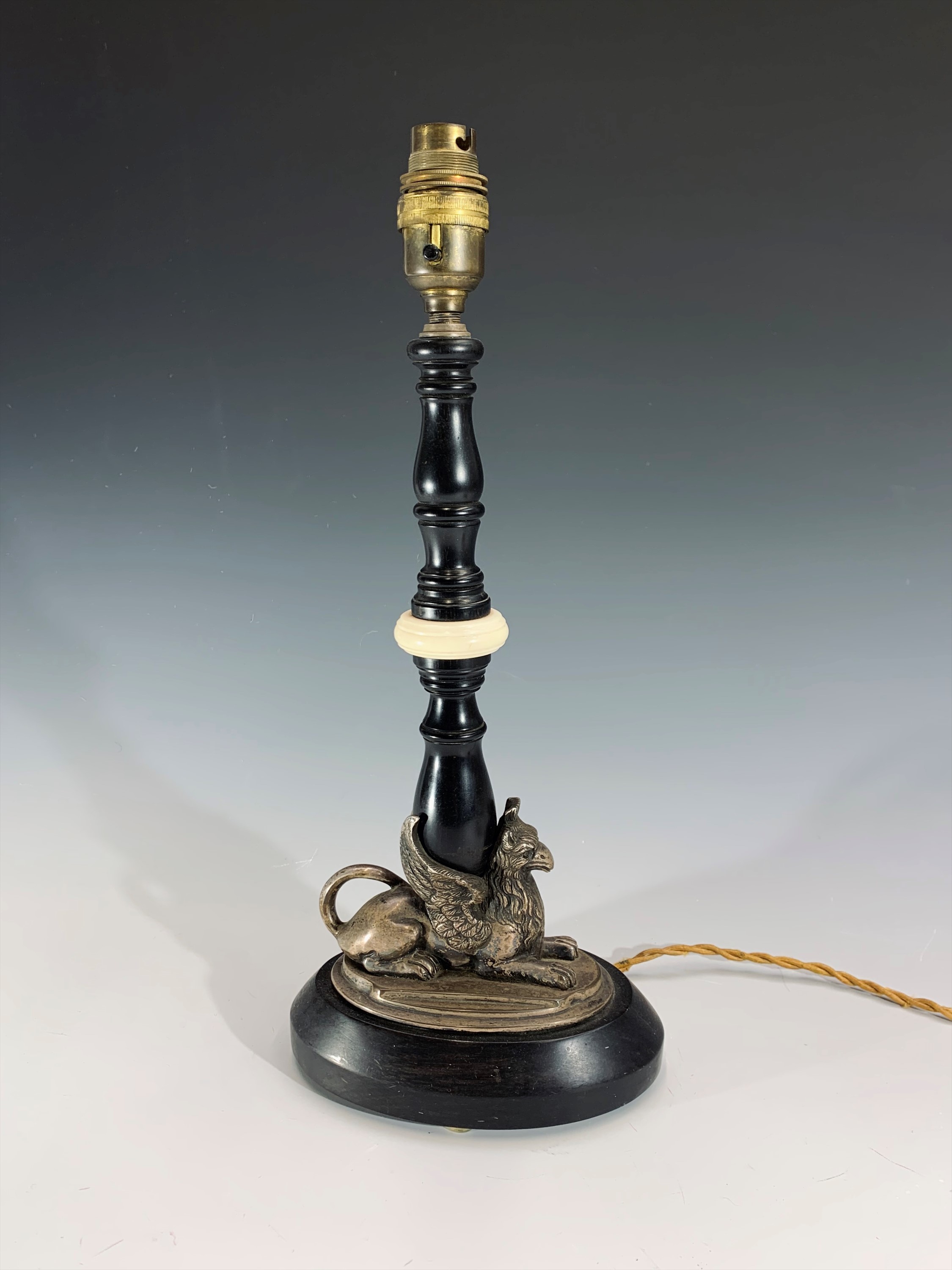 An early 20th century ebonised wood and ivory table lamp, the plated base in the form of a recumbent