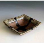 A Janet Leach square dish with ash glazed rim and tenmoku cross, width 15cm, height 4.5cm.