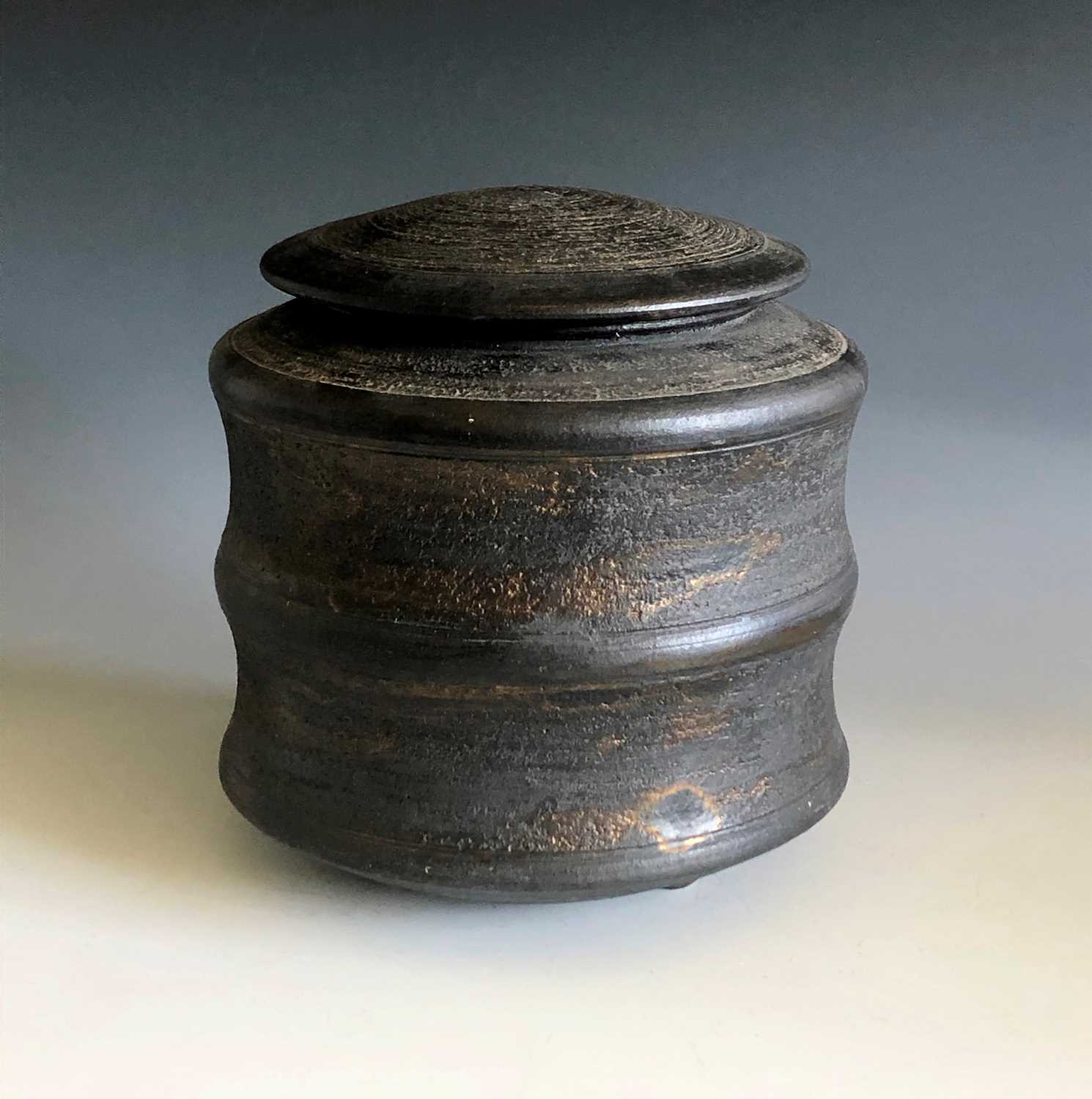 A Jason Wason black stoneware lidded pot with mottled gold glazed and on four domed feet, height