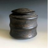 A Jason Wason black stoneware lidded pot with mottled gold glazed and on four domed feet, height