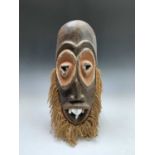 An African carved wood mask of elongated form, inset with four animal teeth, and with string