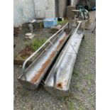 A pair of galvanised metal sectional feeding troughs, on cast trolley wheels. Length 284cm.