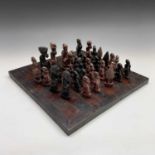 An African hardwood chess set, the pieces carved as figures and trees in natural and stained finish,