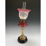 A Victorian brass oil lamp, with cranberry reservoir, on a column support and circular ceramic base,