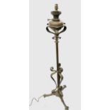 An Arts and Crafts brass standard oil lamp with applied scroll decoration on three feet, converted
