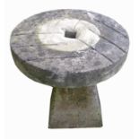 A circular millstone, diameter 54cm, raised on an angular staddle stone base. Height 56cm.