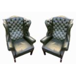 A pair of George III style green leather wing armchairs, by Wade, with a button back, padded and