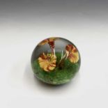 A glass paperweight, with three flowers emerging from a naturalistic coloured base. Width 9.5cm.