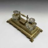 A Victorian brass desk stand with two glass inkwells, a central hinged compartment and pen tray.