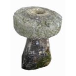 A granite millstone, indistinctly initialled, 52cm diameter, raised on an angled staddle stone base.